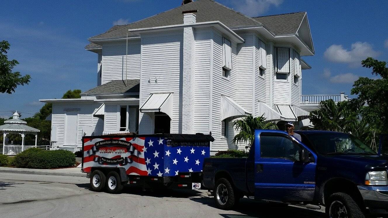 A pickup truck parked in front of a white house with an American flag on it, signaling the need for junk removal services.